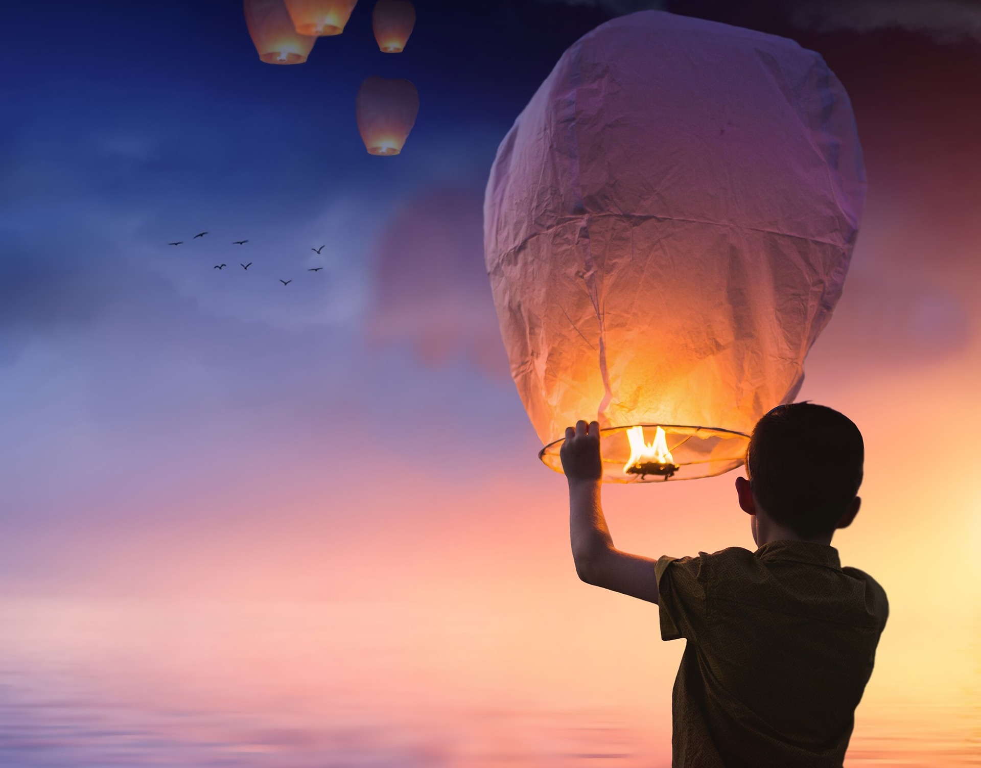 Person lighting a flame in a paper lantern and letting it go up into the sky.