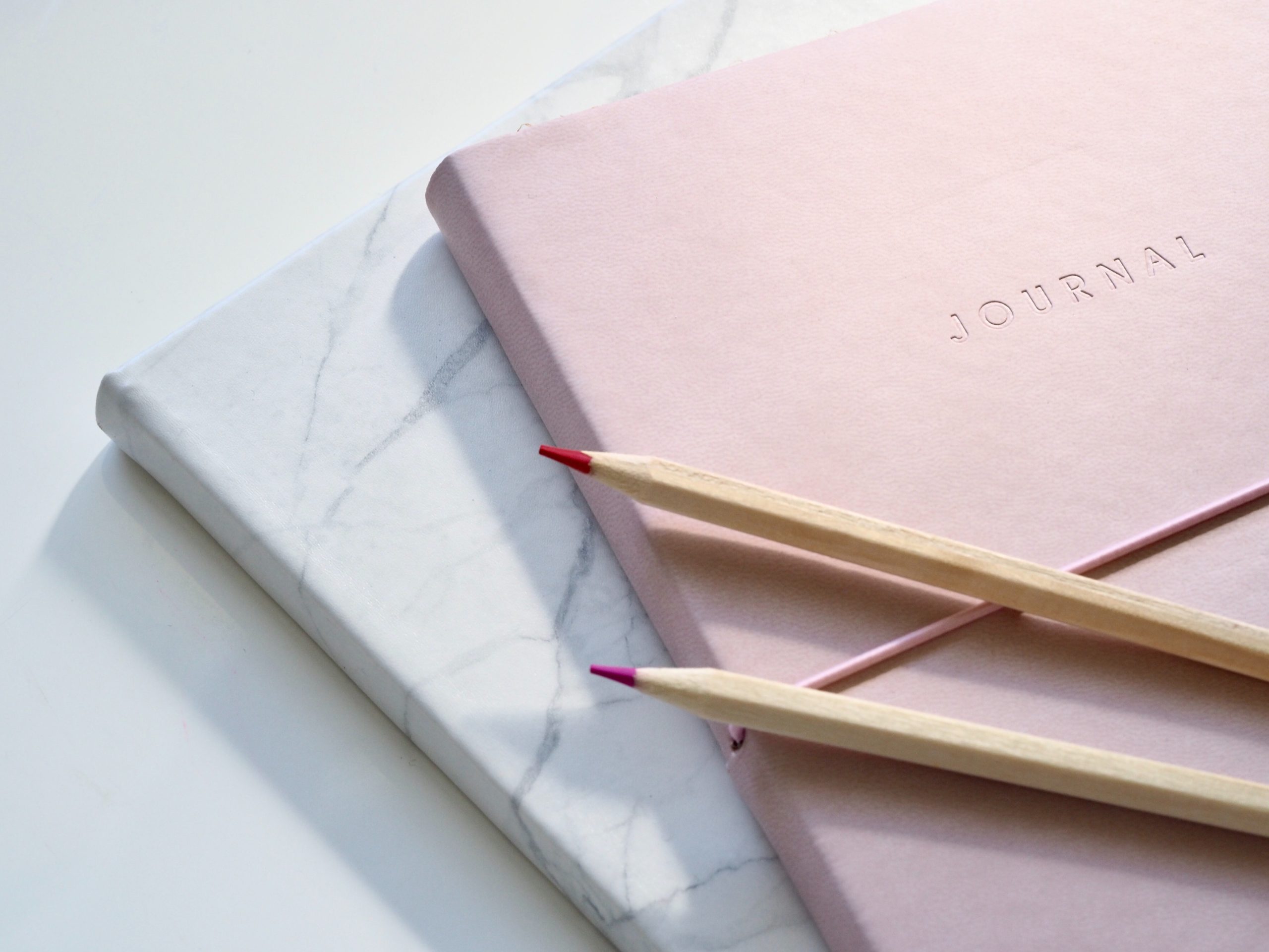 One pink and one marble journal stacked on top of one another with two pink pencil crayons.