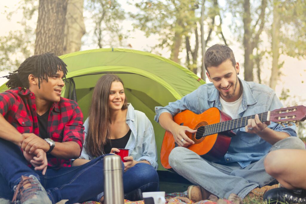 Three people sitting on ground with tent behind them.