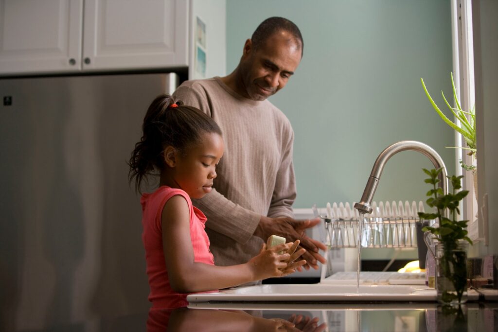 Father and daughter washing hands at kitchen sink.