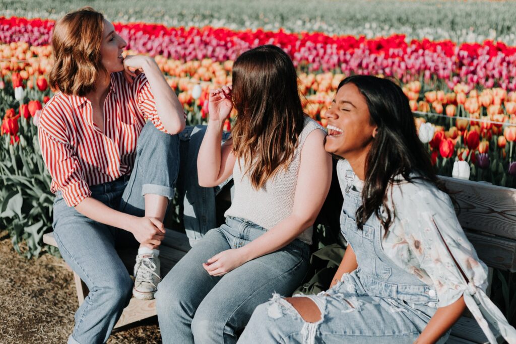 Group of three women sitting on a bench in front of garden.