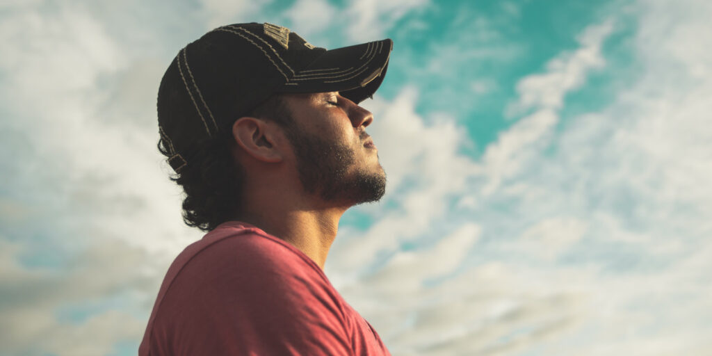 Man outside wearing hat with eyes closed and head tilted towards the sky.