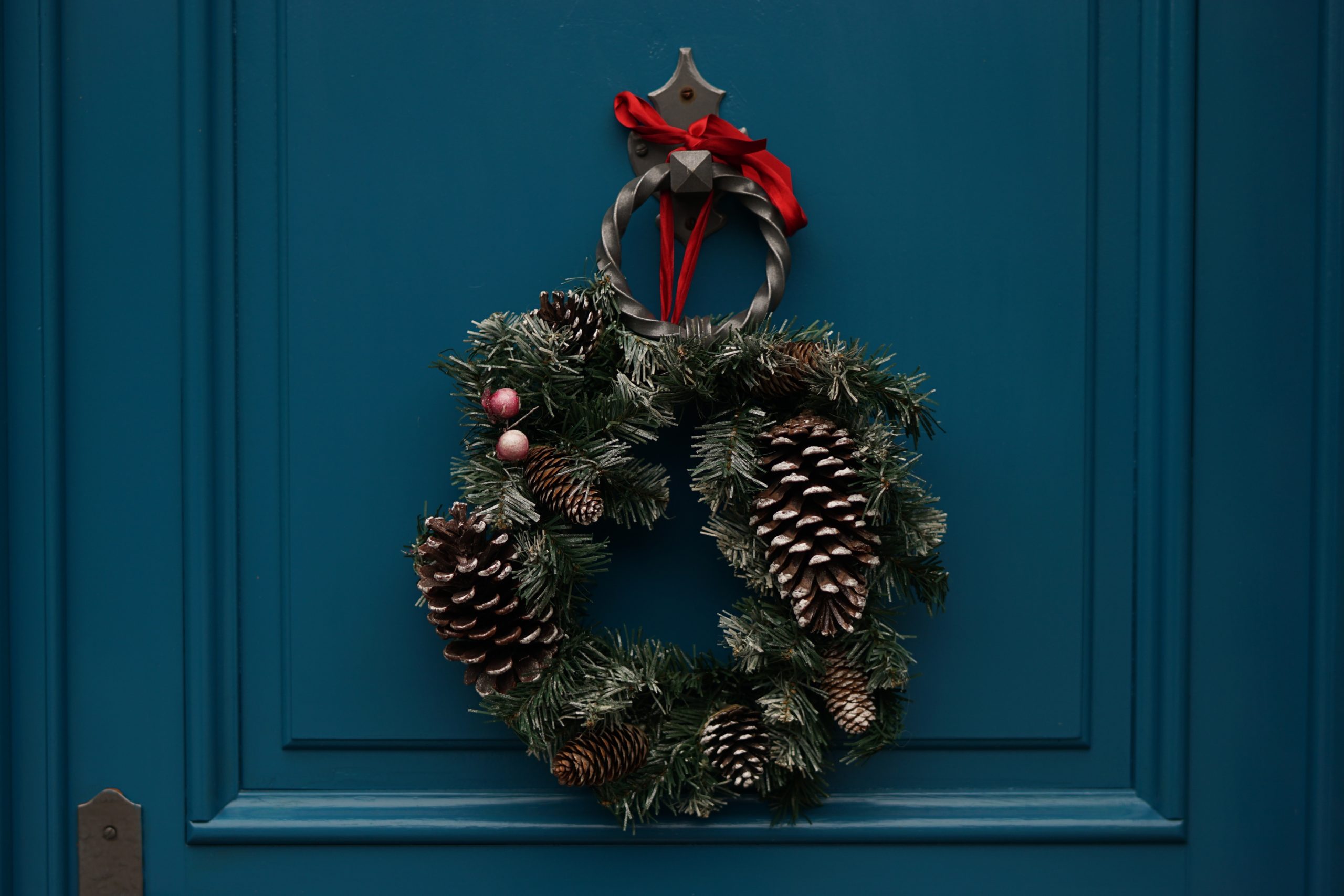 A Christmas wreath hanging on a teal door.