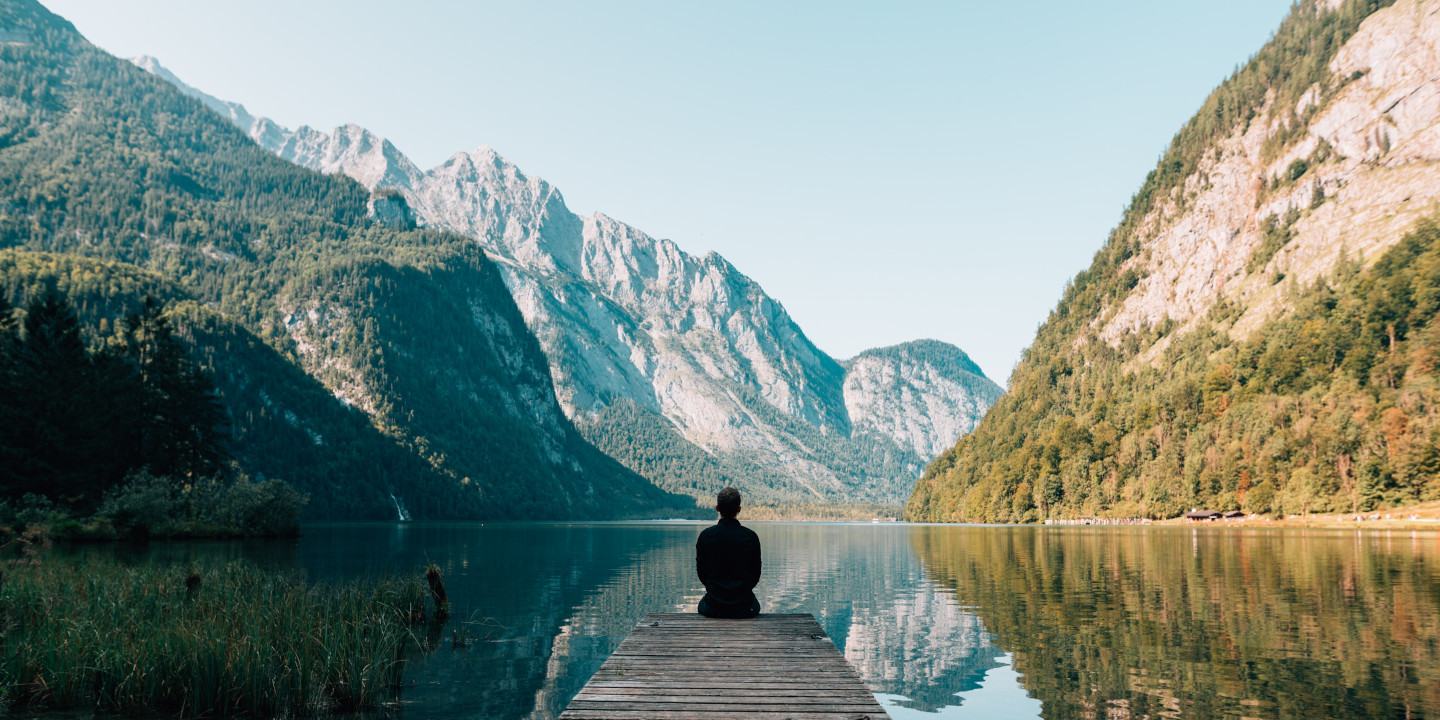 Man in recovery sitting on dock by lake and mountains.