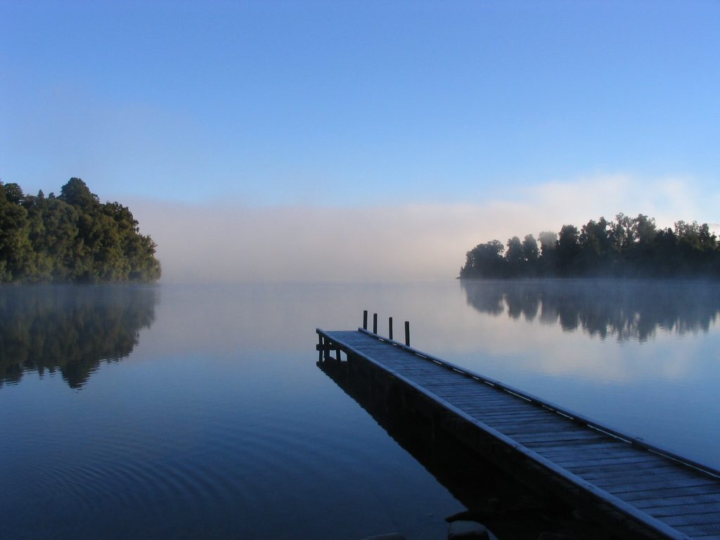 Dock on lake with trees on either side.