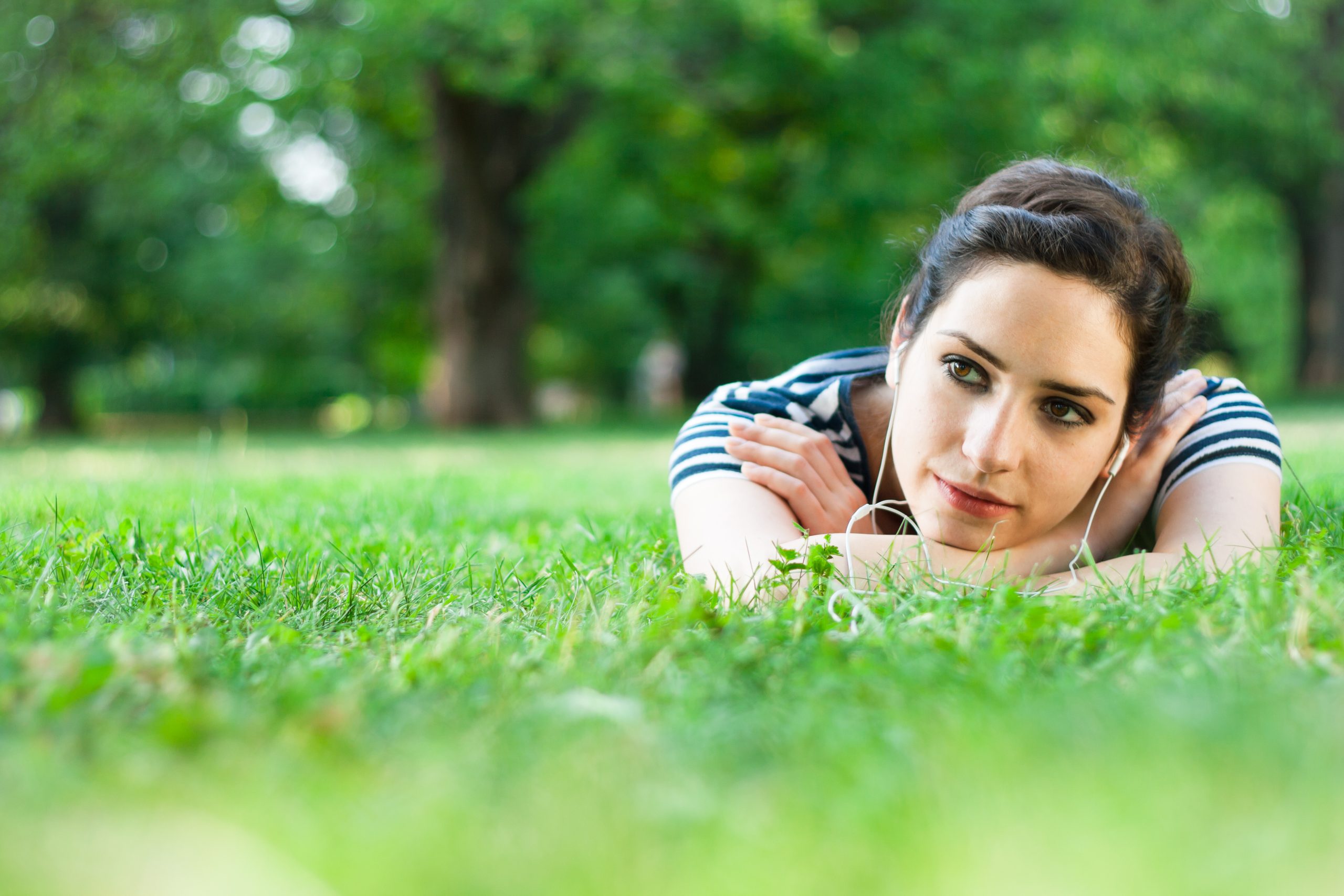 Women wearing headphones and laying in the grass in a park.
