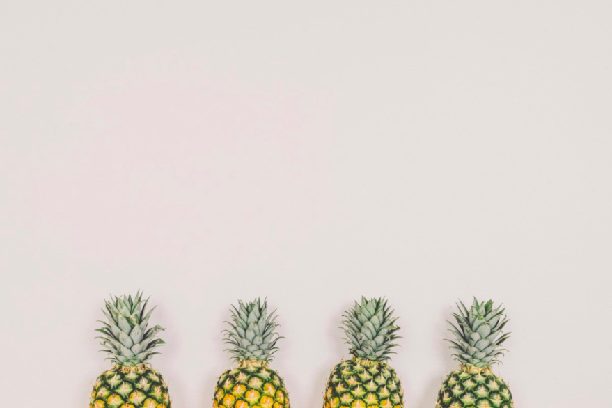 Four pineapples against white wall.