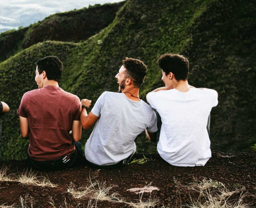 A group of friends laughing atop a hill with a mountains in the distance.