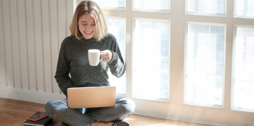 Woman sitting on floor by a window on a laptop.