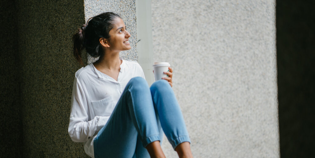 Woman sitting near window holding a cup of coffee.