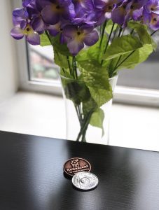 Renascent addiction treatment centre recovery medallion and bouquet of purple flowers.