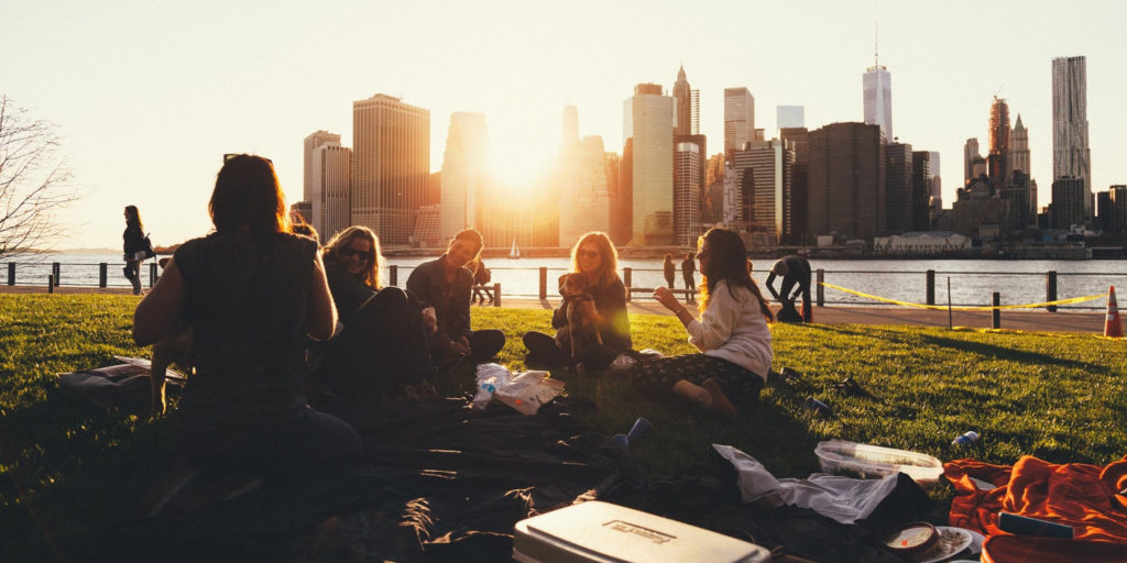 Group of friends having picnics sitting on the grass with view of city skyline.