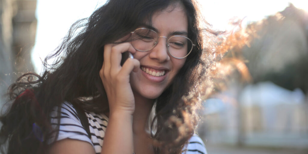 Young woman wearing glasses, smiling and talking on phone.