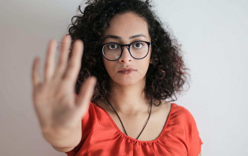 A person wearing glasses looking at the camera and holding out their right hand to symbolize "stop"