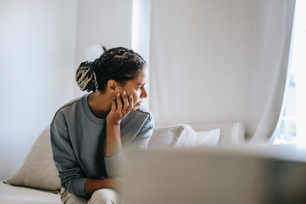 Person sitting on couch looking out the window with the chin resting on their hand.
