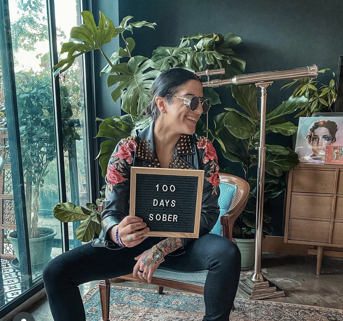 Julie sitting and holding an sign that says '100 Days Sober'