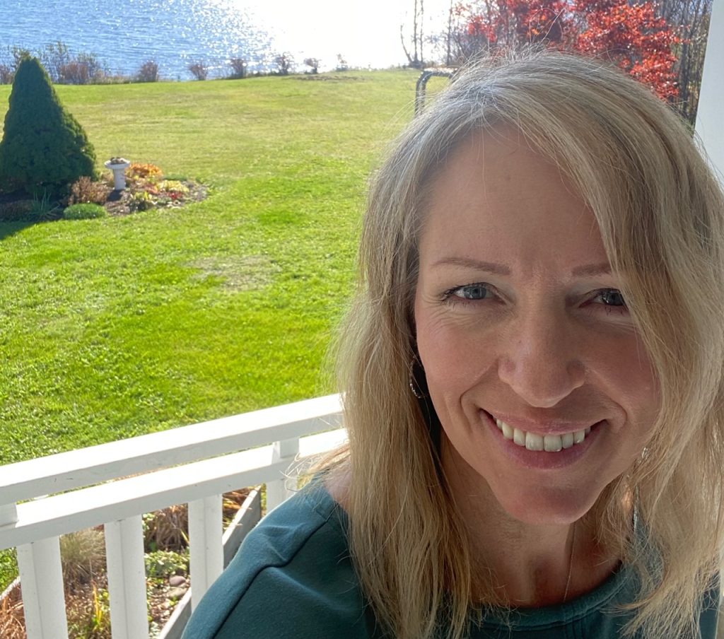 Tammi sitting on deck with nice yard and lake in the background