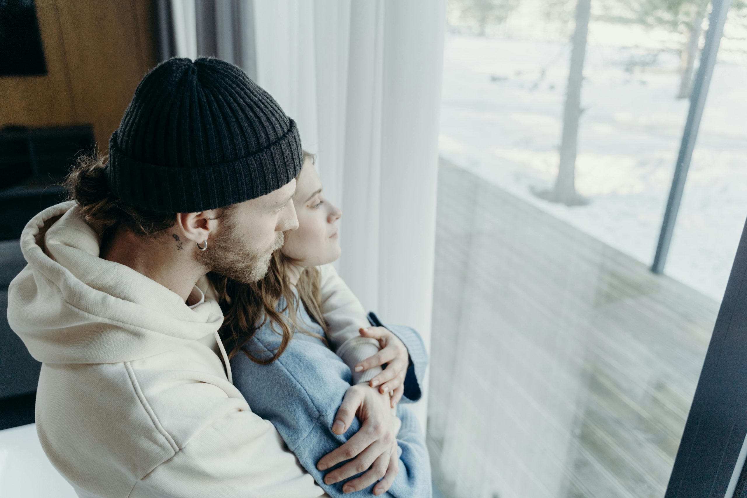Two people standing looking out window in embrace