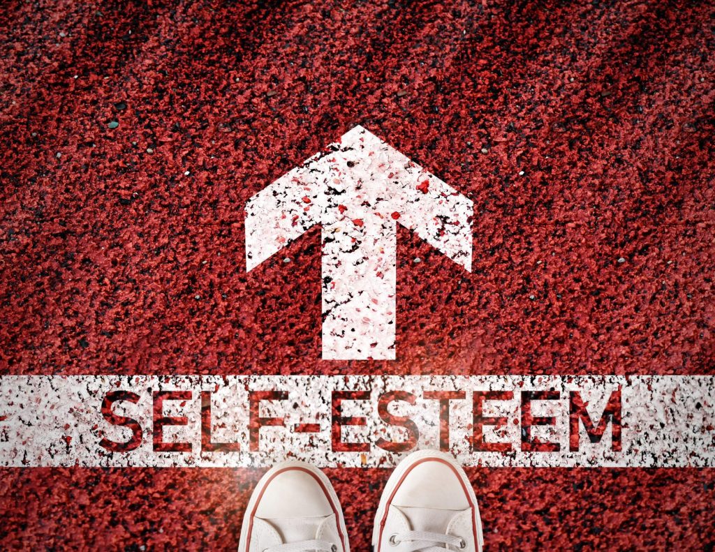 Shoes at the start line of a track with the words "Self-esteem" written on the track.