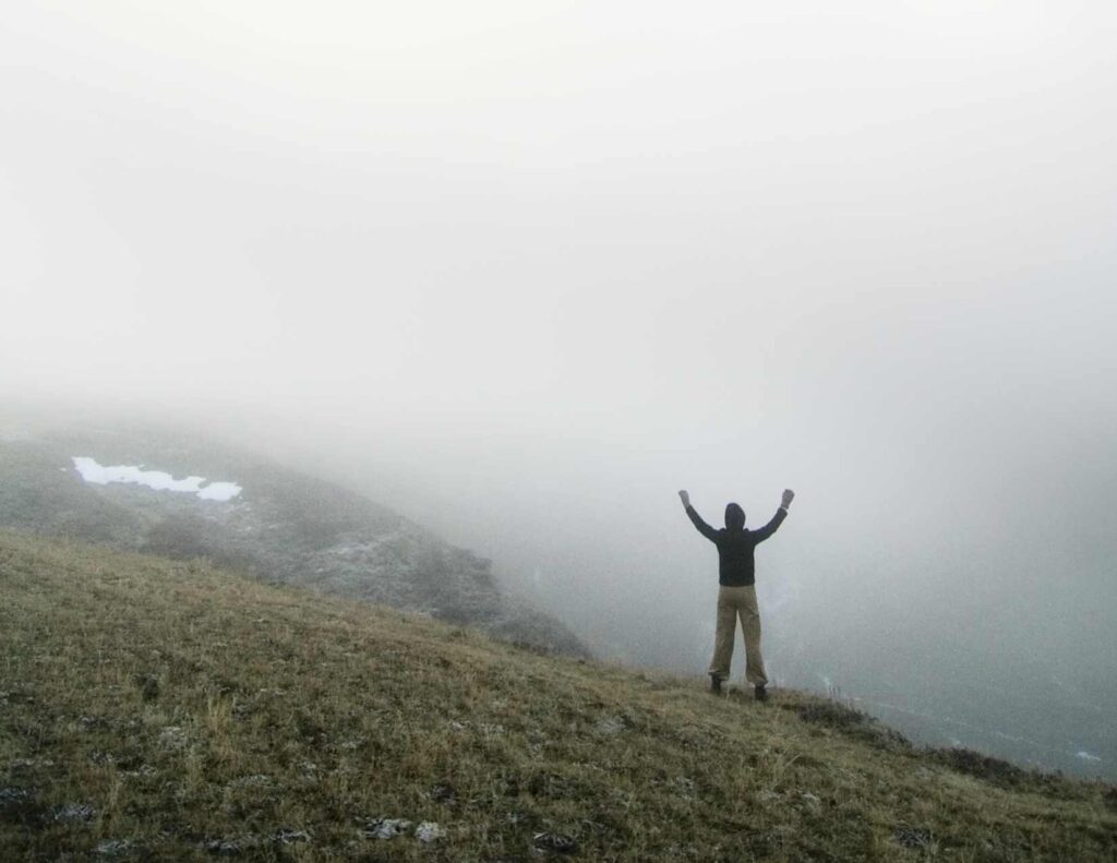 Person standing on hill with hands outstretched